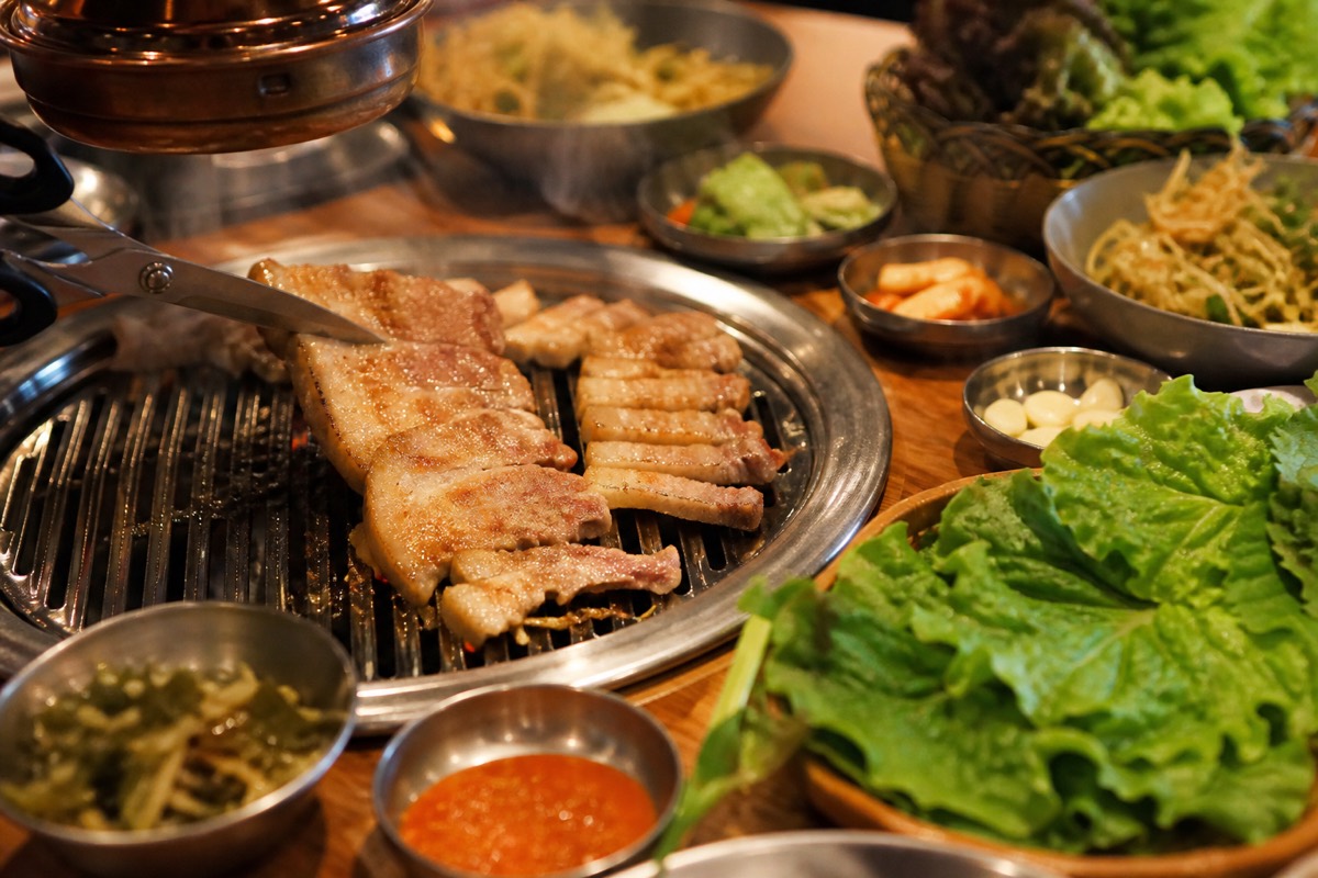 Pork belly grilling on a Korean barbecue table with side dishes
